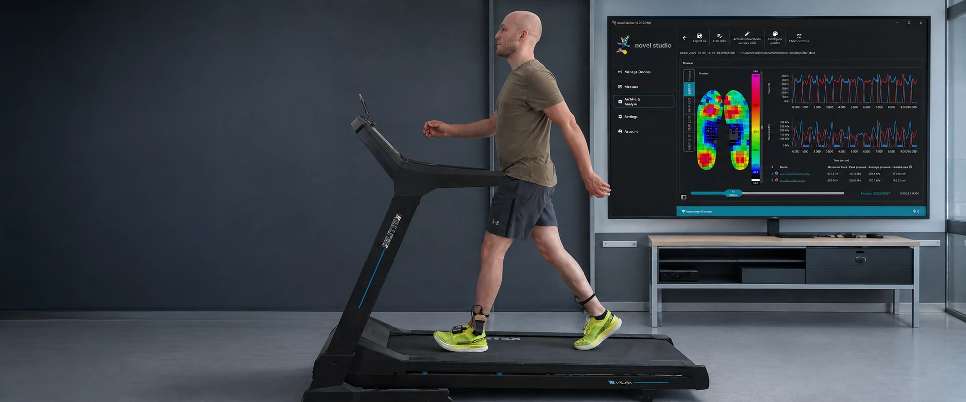 Man walking on a treadmill wearing pedar sensors, with a software monitor behind him in a gait lab